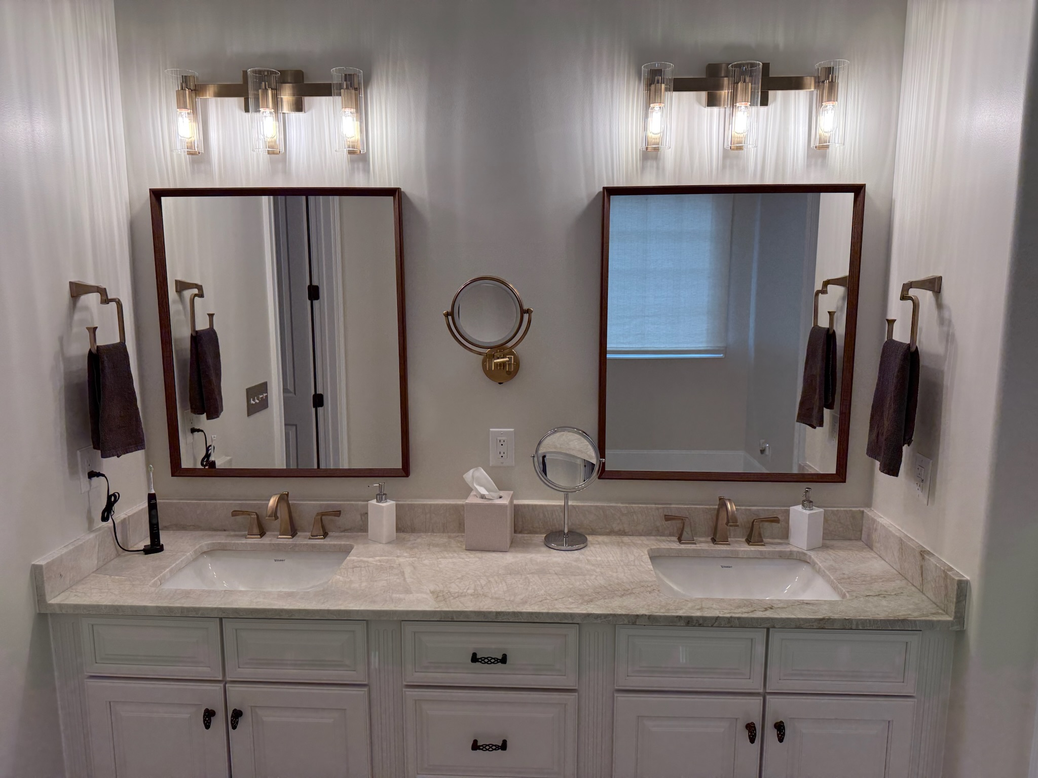 Double vanity with cream raised-panel cabinets, cherry-framed mirrors, brushed gold faucets and sconces in an Upstate SC bathroom