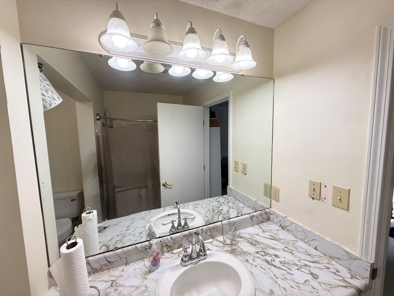 Before: vanity area of the original primary bathroom in the Ketner home in Simpsonville, SC with builder-grade light bar and marble-look top prior to remodel - photo 3